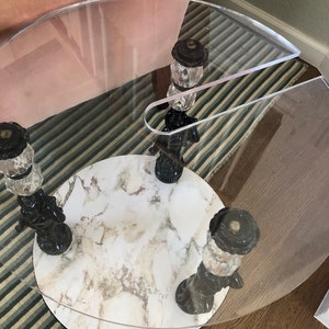May include: A round, clear glass table with a white marble top. The table has three black and gold legs with decorative finials.