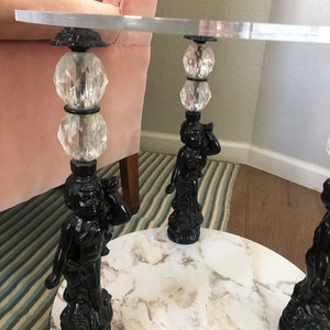 May include: A round, white marble table top with three black cherub-shaped legs. Each leg has a crystal ball and a black metal base.