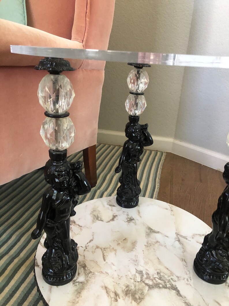 May include: A round, white marble table top with three black cherub-shaped legs. Each leg has a crystal ball and a black metal base.