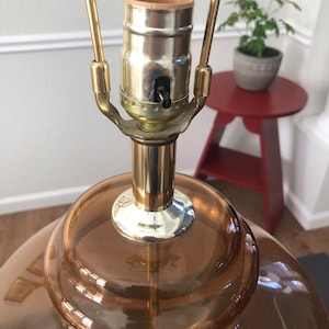 Może przedstawiać: Złota lampa stołowa z brązowym abażurem ze szkła. Lampa ma prosty design i klasyczny wygląd.
