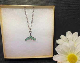 May include: A silver necklace with a green mermaid tail pendant. The pendant is set with small green stones. The necklace is in a small gift box.