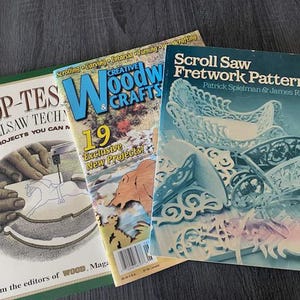 May include: Three woodworking magazines: "Shop-Tes Scrollsaw Techniques", "Creative Woodcrafts", and "Scroll Saw Fretwork Patterns". The magazines feature scroll saw projects and patterns, with colorful covers and text.