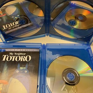 May include: Blu-ray disc set of the animated film "My Neighbor Totoro" in a blue case. The cover art features the film's title and a depiction of Totoro. The discs are gold and reflect light.