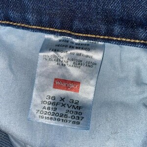 May include: Close-up of a blue denim jeans label. The label reads "Wrangler" and includes size information: 36 x 32. The label also indicates the jeans were made in Mexico and lists the fabric composition.