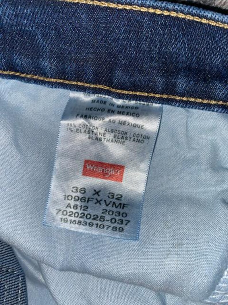 May include: Close-up of a blue denim jeans label. The label reads "Wrangler" and includes size information: 36 x 32. The label also indicates the jeans were made in Mexico and lists the fabric composition.
