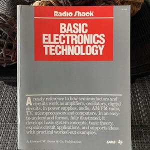 May include: A vintage "Radio Shack" book titled "Basic Electronics Technology." The cover is gray with a red rectangle containing white text. The book provides a reference on semiconductors, circuits, and more. A Howard W. Sams & Co. Publication.