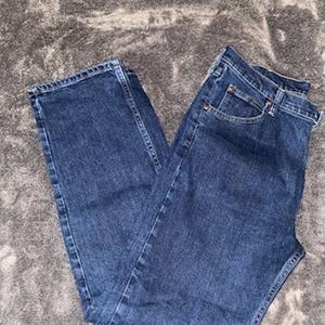May include: Dark blue denim jeans with a classic five-pocket design. The jeans are folded and appear unworn, showcasing a medium wash and traditional stitching details. A staple for casual wear.