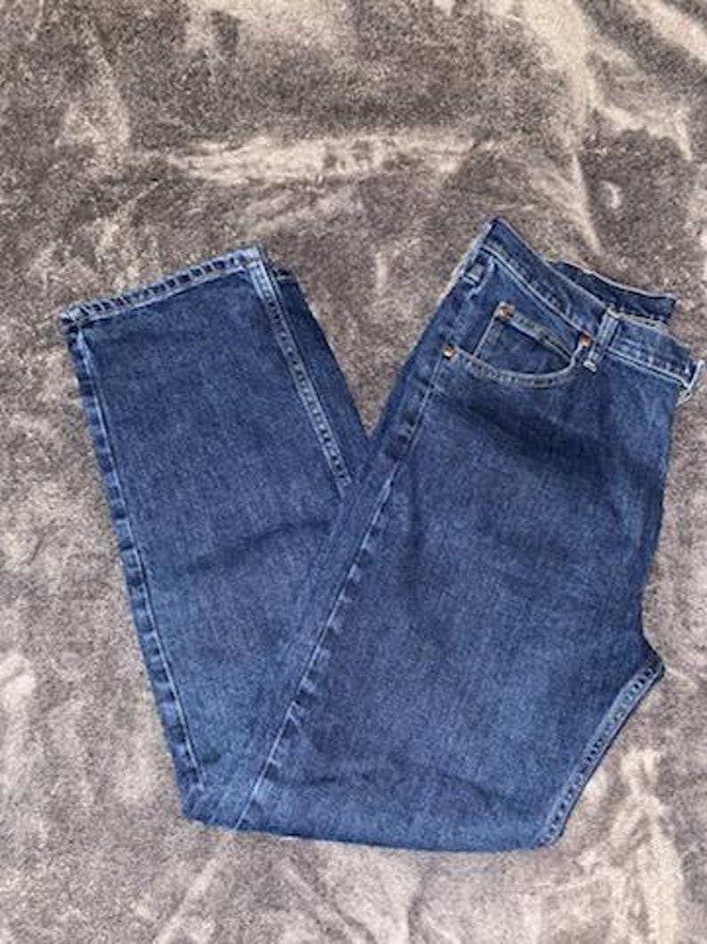 May include: Dark blue denim jeans with a classic five-pocket design. The jeans are folded and appear unworn, showcasing a medium wash and traditional stitching details. A staple for casual wear.