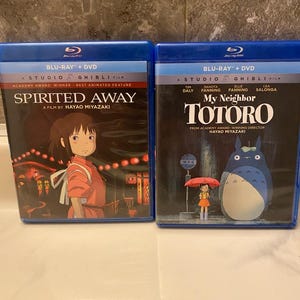 May include: Two Blu-ray + DVD combo packs of Studio Ghibli films. The first is "Spirited Away" with a girl in an orange outfit. The second is "My Neighbor Totoro" with the title character and a girl with an umbrella.