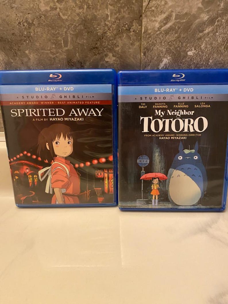 May include: Two Blu-ray + DVD combo packs of Studio Ghibli films. The first is "Spirited Away" with a girl in an orange outfit. The second is "My Neighbor Totoro" with the title character and a girl with an umbrella.