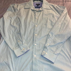 May include: A light blue button-down shirt with vertical white stripes. The long-sleeved shirt has a chest pocket, a collar, and buttoned cuffs with a blue trim. The shirt is hanging on a black hanger.