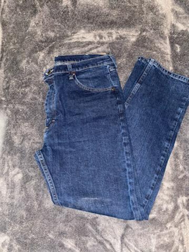 May include: Dark blue denim jeans. The jeans have a classic five-pocket design, a button and zipper closure, and belt loops. The denim has a slightly faded appearance, with subtle wear marks.