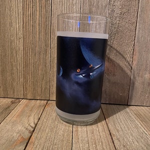 May include: A clear glass tumbler with a frosted finish features a printed design of a spaceship flying through a nebula with a blue planet in the background.
