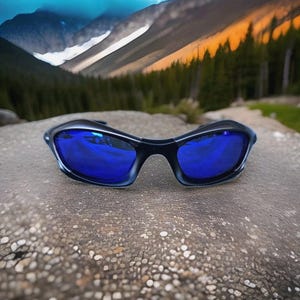 Puede incluir: Gafas de sol negras con lentes azules reflectantes sobre una roca texturizada. Las gafas de sol tienen un dise&ntilde;o deportivo, con una montura curvada y un aspecto elegante y moderno.