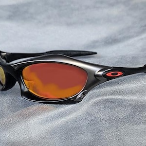 Puede incluir: Gafas de sol deportivas con montura negra y lentes tintadas en naranja. Las gafas tienen un dise&ntilde;o elegante y moderno con un logotipo rojo en la patilla. Las lentes son curvadas y ofrecen cobertura total.