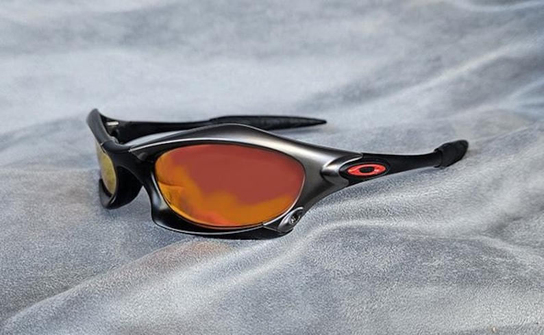 Puede incluir: Gafas de sol deportivas con montura negra y lentes tintadas en naranja. Las gafas tienen un dise&ntilde;o elegante y moderno con un logotipo rojo en la patilla. Las lentes son curvadas y ofrecen cobertura total.