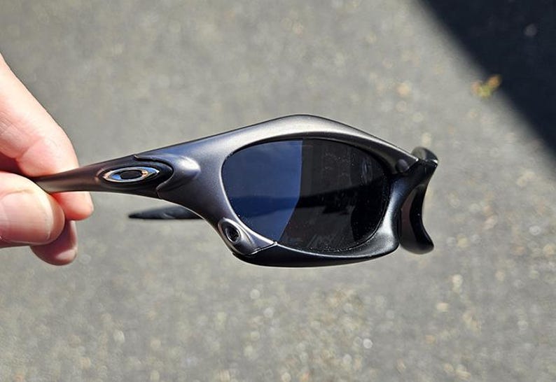 Peut inclure: Lunettes de soleil grises avec des verres fonc&eacute;s. Les lunettes ont une monture incurv&eacute;e et un petit logo argent&eacute; sur la branche. Les verres sont sombres et prot&egrave;gent du soleil.