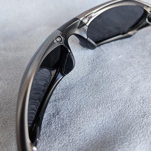 Peut inclure: Gros plan sur des lunettes de soleil avec une monture m&eacute;tallique. Les verres sombres contrastent avec le m&eacute;tal argent&eacute;. Les branches sont incurv&eacute;es et le design int&egrave;gre des accents noirs. L'esth&eacute;tique g&eacute;n&eacute;rale est moderne et &eacute;l&eacute;gante.