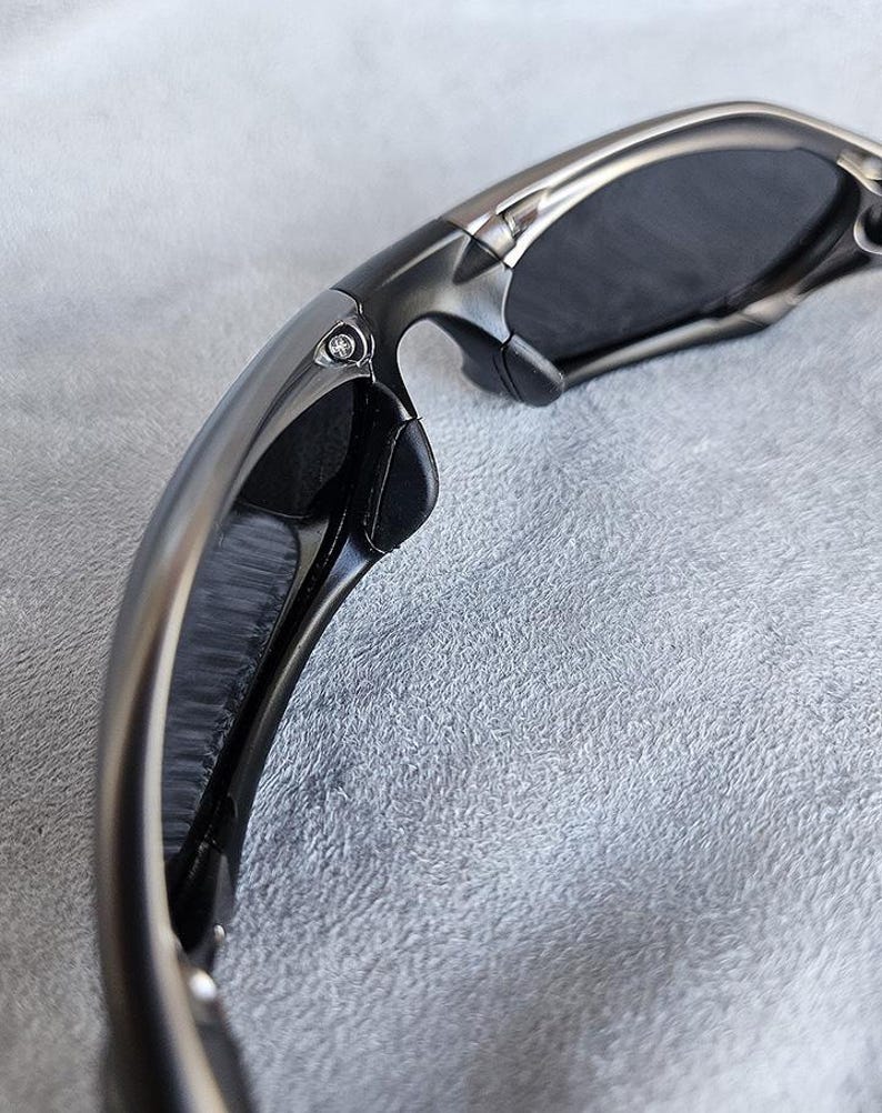Peut inclure: Gros plan sur des lunettes de soleil avec une monture m&eacute;tallique. Les verres sombres contrastent avec le m&eacute;tal argent&eacute;. Les branches sont incurv&eacute;es et le design int&egrave;gre des accents noirs. L'esth&eacute;tique g&eacute;n&eacute;rale est moderne et &eacute;l&eacute;gante.
