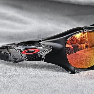 May include: Black sports sunglasses with a wraparound design. The lenses have a gradient of yellow to orange, reflecting the surroundings. A red logo is visible on the frame.