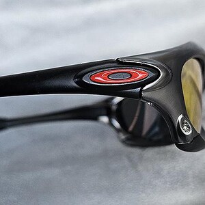 Puede incluir: Primer plano de gafas de sol negras con un logotipo rojo y blanco en la patilla. Las lentes son amarillas y la montura es negra mate. Las gafas de sol est&aacute;n en &aacute;ngulo, mostrando el lateral y la parte delantera.