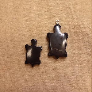 May include: Two black turtle-shaped pendants with silver jump rings. The larger pendant is about 5 cm long and the smaller pendant is about 2.5 cm long.