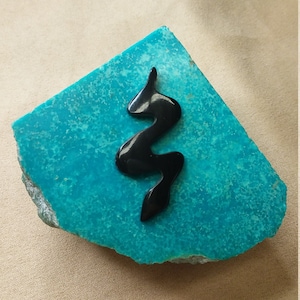 Può includere: Una pietra turchese con un design nero astratto ondulato.