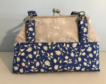 Blue Cream Floral Kiss Lock Cross Body Handbag. Magnetic Outside Pocket. 6 Card Pockets. Adjustable Strap, Nickel Hardware.