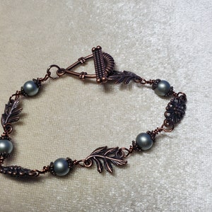 May include: A copper wire bracelet with gray beads and leaf charms. The bracelet has a toggle clasp.