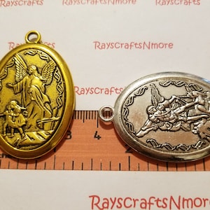 May include: Two oval-shaped metal pendants with religious imagery. The pendant on the left is gold and features an angel with wings, a halo, and a child. The pendant on the right is silver and features an angel with wings, a halo, and a sword. Both pendants are approximately 1 inch in diameter.