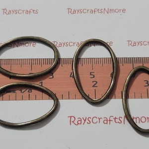Puede incluir: Cuatro anillos ovalados de bronce antiguo de diferentes tamaños, dispuestos sobre una regla. El texto "RayscraftsNmore" es visible en el fondo. Medidas en centímetros.