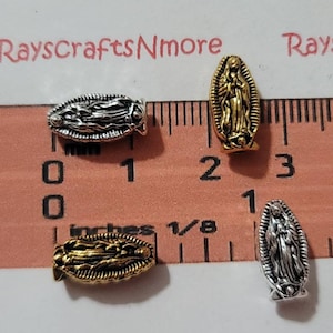 May include: Four silver and gold-toned metal charms featuring an image of the Virgin Mary. The charms are about 1 inch long and are displayed on a ruler.