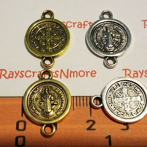 May include: Four metal Saint Benedict connector charms. Two are gold-toned, and two are silver-toned. Each charm is round with a detailed religious design and two small loops for attaching to other items. A ruler is in the image.