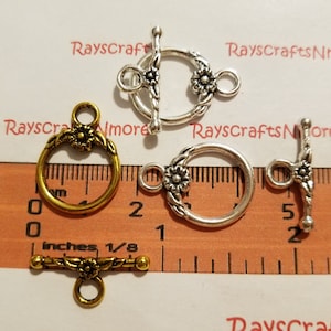 May include: An assortment of metal toggle clasps in gold and silver tones. The clasps feature floral designs and are shown with a ruler for size reference. The text "RaysCraftsNmore" is visible in the background.