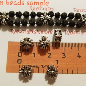 May include: A sample of 4mm beads. The image shows several silver-colored, cross-shaped beads, some strung on a black beaded strand. A ruler with millimeter markings is included for size reference. The text "4mm beads sample" is visible.