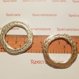 Puede incluir: Dos anillos de metal plateado martillado con bordes irregulares. Los anillos están colocados junto a una regla, con el texto "RaysCraftsNmore" visible en el fondo. Estos anillos son adecuados para la fabricación de joyas o proyectos de artesanía. Miden unos 3 cm de diámetro.
