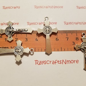 Puede incluir: Tres medallas de San Benito plateadas con crucifijos. Las medallas miden aproximadamente 3,8 cm de alto y llevan las palabras "INRI" en la parte superior de la cruz.