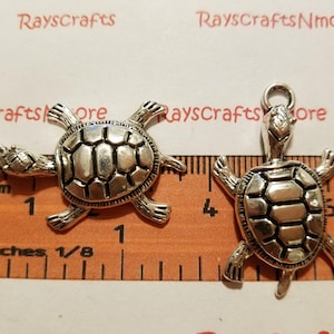 May include: Two silver turtle charms with a detailed shell design. The charms are approximately 2.5 cm in size and have a loop for attaching to jewellery or other crafts.