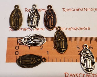 Puede incluir: Un conjunto de dijes metálicos ovalados con la Virgen María. Los dijes están en varios acabados metálicos, incluyendo bronce, plata y cobre. Cada dije tiene un pequeño lazo en la parte superior para sujetarlo a joyas u otras manualidades.