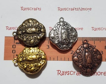 Puede incluir: Cuatro dijes de metal con la imagen de la Virgen de Guadalupe en acabados de latón antiguo, oro brillante, plata y cobre. Cada dije tiene un borde ornamentado en forma de cuatrifolio con volutas. Una regla muestra que miden 3,2 cm de ancho.