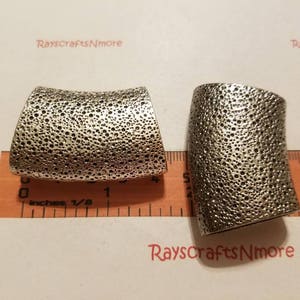 Puede incluir: Dos componentes de joyería de metal plateado texturizado. Las piezas son curvas, con una superficie porosa y picada. Se colocan sobre una regla marcada en pulgadas. El texto "RaysCraftsNmore" es visible.