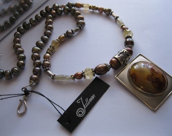 May include: A brown and silver necklace with a large, rectangular pendant featuring a brown agate stone. The necklace is made with brown pearls, silver beads, and gold beads. The pendant has a silver frame and a brown agate stone in the centre. The necklace has a black tag with the word "Julloon" written on it.