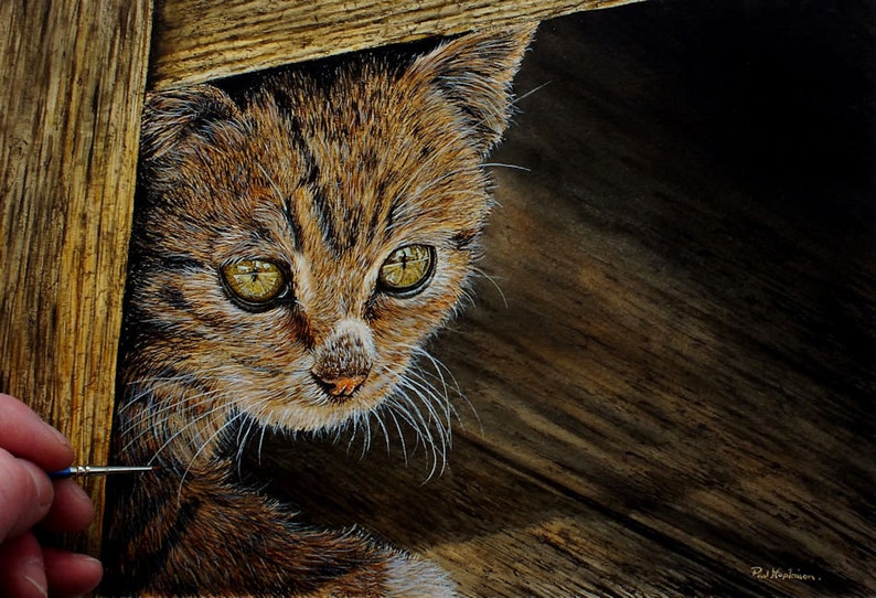 Paul working on the last details for a painting of a tabby kitten underneath a chair.  The overall colour is brown, as the cat is a brown tabby, it is under a chair and on floorboards.  He has painted it in fine details.