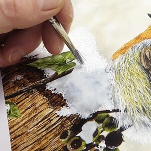Paul is working with an old bristly brush and is dabbing opaque white paint on the background he has painted for the snow.