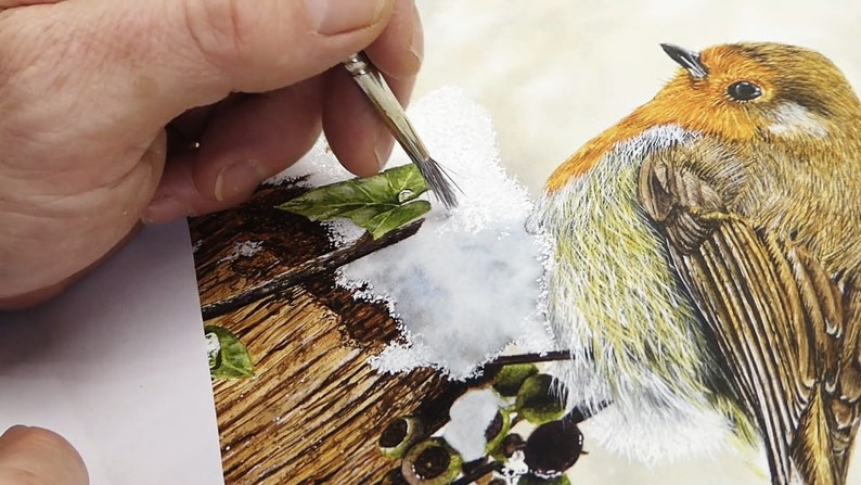 Paul is working with an old bristly brush and is dabbing opaque white paint on the background he has painted for the snow.