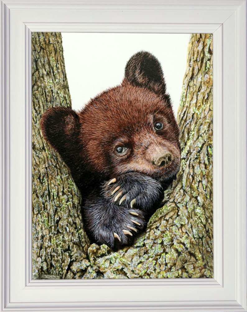The completed bear cub painting in a white frame.  The cub is nestled into a crook in a tree, with its paws under its face.  It has chocolate brown fur on it's face, but the ears and paws are a darker purply brown.  The tree bark is very rough.