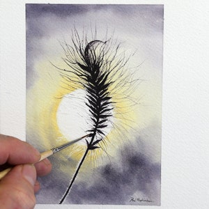 A silhouette of a grass seed head being painted by Paul against the background of the sun in a dark mauve coloured sky. The seed head has lots of wispy hairs surrounding it, and creating a stunning effect against the background