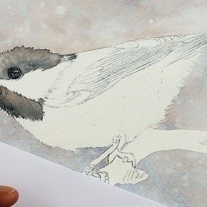 A set of 4 work in progress photos of the chickadee as it is being painted.  In this photo, Paul has painted the tiny black eye, and is applying a wash to the black parts of the head.  The snowy background has already been added.