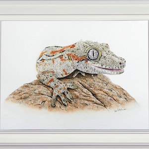 The finished lizard painting in a white frame.  This is a pale brown animal with russet orange patterns on its skin.  It is on a piece of stone, in similar colours.