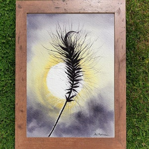 The grass seed head silhouette painting in a wooden frame laid on a lawn.